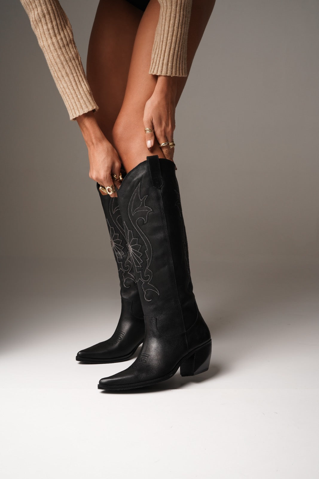 Tall black cowboy boots with pointed toes, angled heels, and subtle black-on-black Western embroidery along the shaft. A sleek and edgy twist on a classic silhouette, perfect for bold, versatile styling.