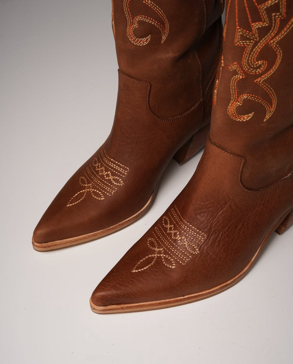 Tall tan cowboy boots with pointed toes, angled heels, and subtle Western embroidery along the shaft. A sleek and edgy twist on a classic silhouette, perfect for bold, versatile styling.