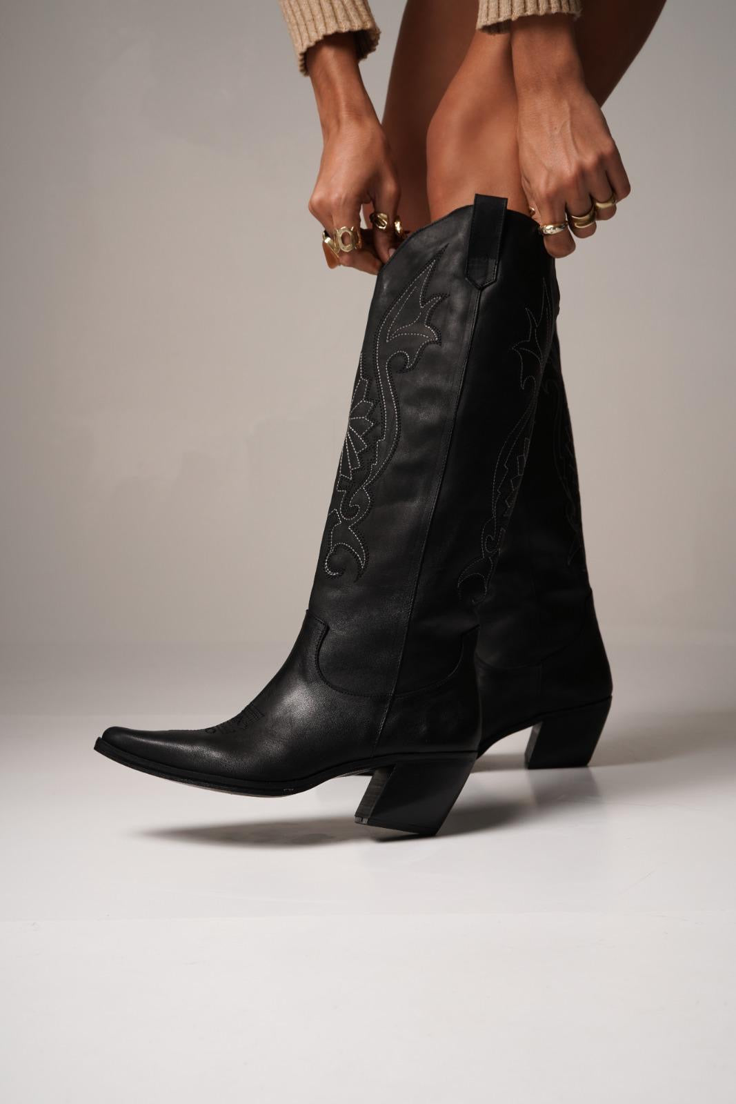 Tall black cowboy boots with pointed toes, angled heels, and subtle black-on-black Western embroidery along the shaft. A sleek and edgy twist on a classic silhouette, perfect for bold, versatile styling.