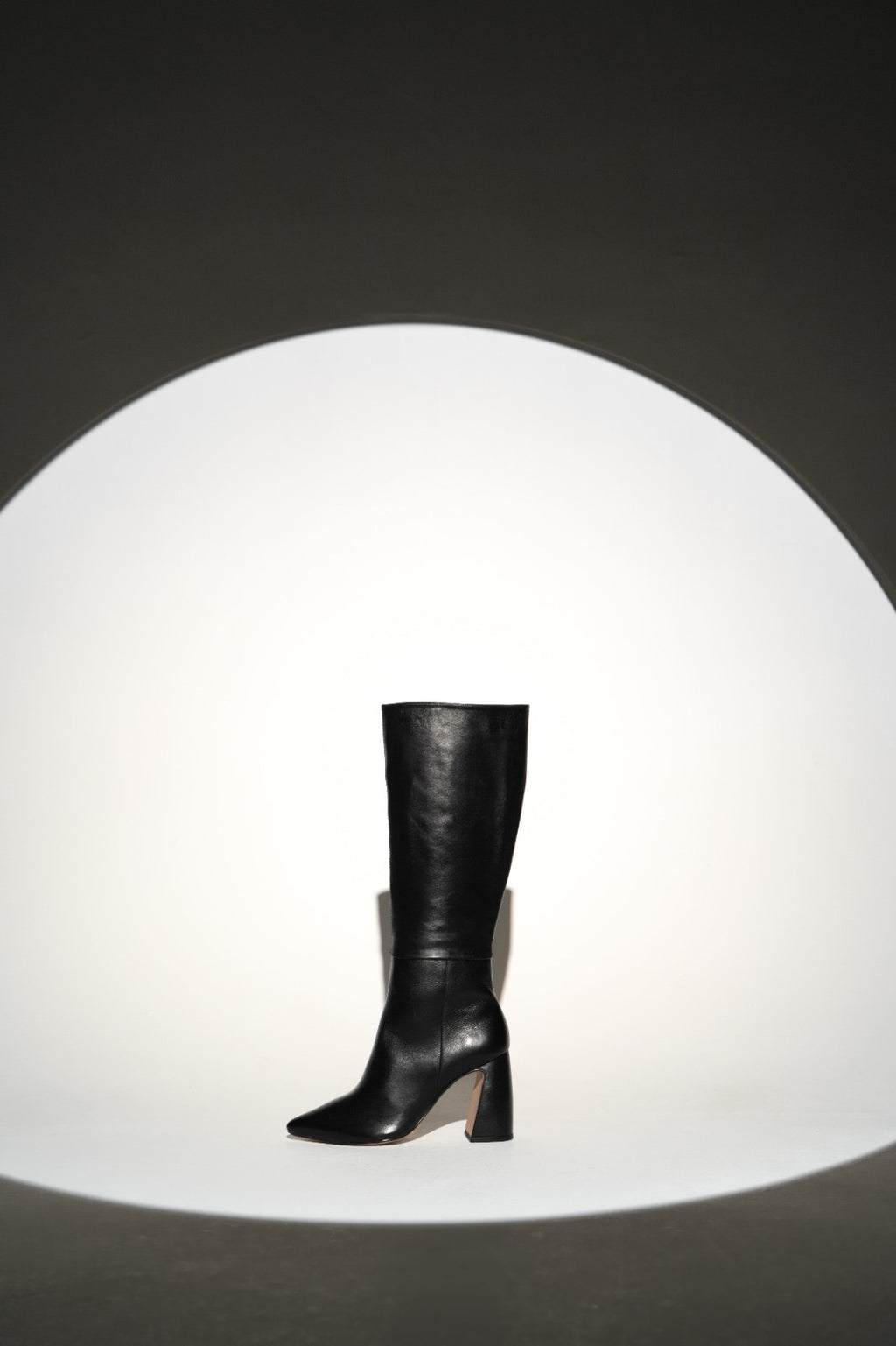 Sleek black knee-high leather boot with a pointed toe and sturdy high block heel. A minimalist and elegant design perfect for chic, everyday wear or polished evening looks.