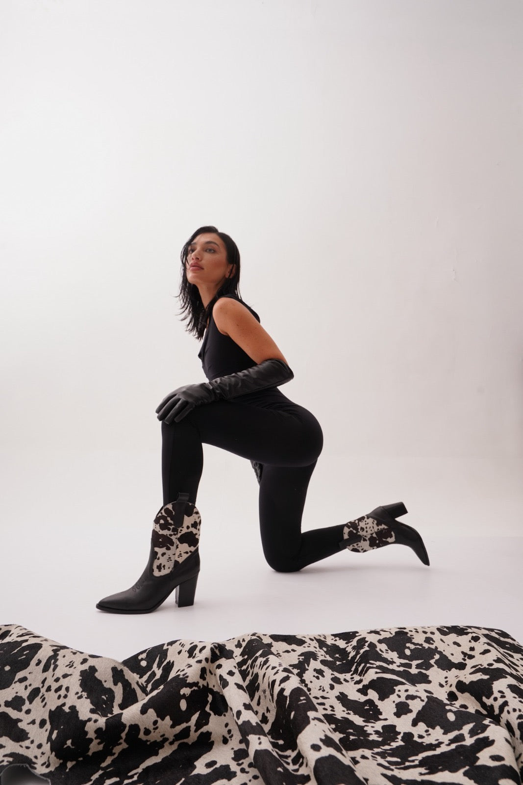 Black leather ankle boots featuring warm black-and-white cow-print uppers, wooden stacked heels, and engraved detailing. A bold Western statement for stylish day-to-night wear.