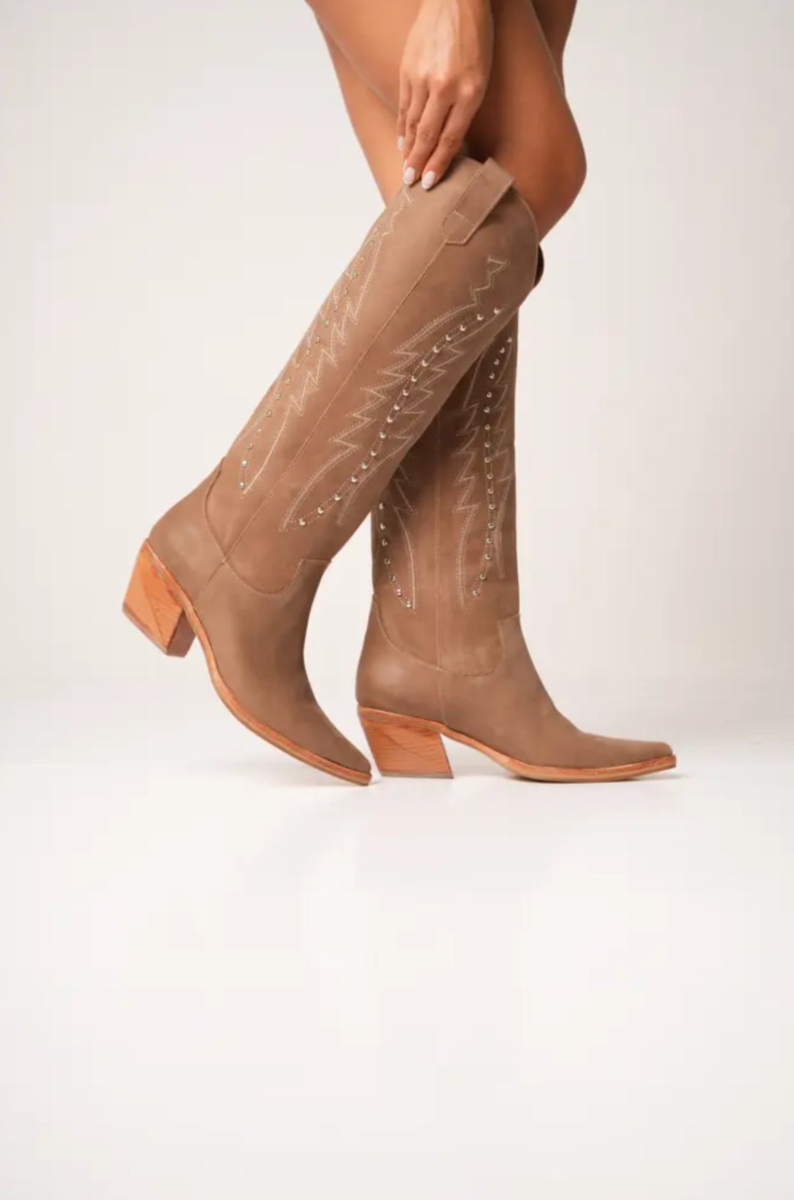 Classic tall tan cowboy boots with pointed toes, angled block heels, and intricate tonal embroidery on the shaft. A timeless Western silhouette with a sleek, all-black finish for versatile, edgy styling.