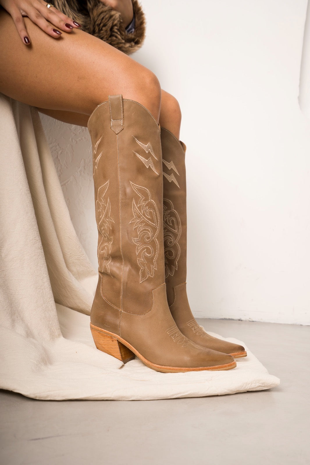 Classic tall tan cowboy boots with pointed toes, angled block heels, and intricate tonal embroidery on the shaft. A timeless Western silhouette with a sleek, all-black finish for versatile, edgy styling.