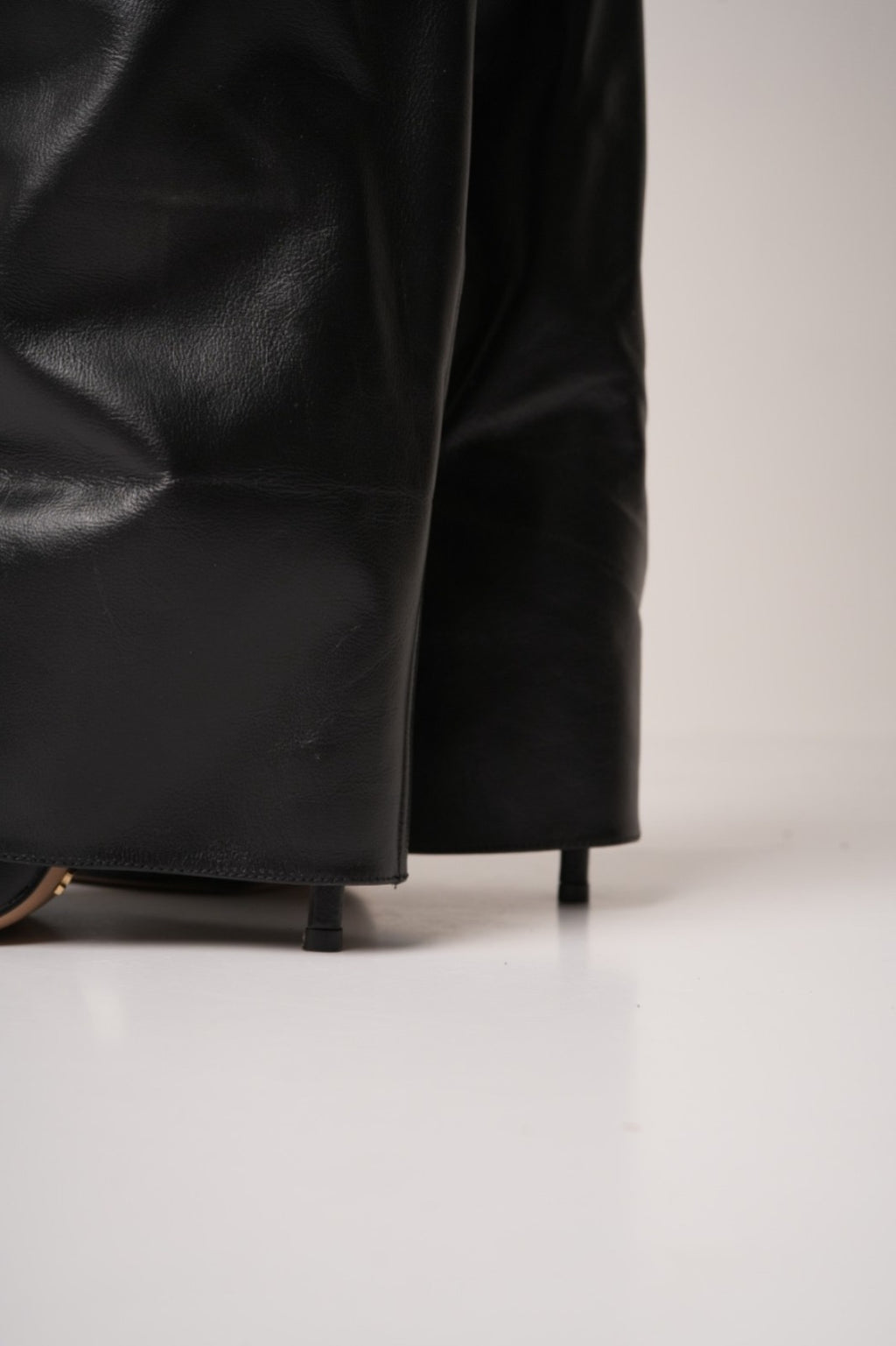 Elegant black knee-high stiletto boots with pointed toes, slouchy leather texture, and a gold padlock detail at the ankle. These statement boots blend luxury and edge—perfect for high-fashion looks or a bold night out.