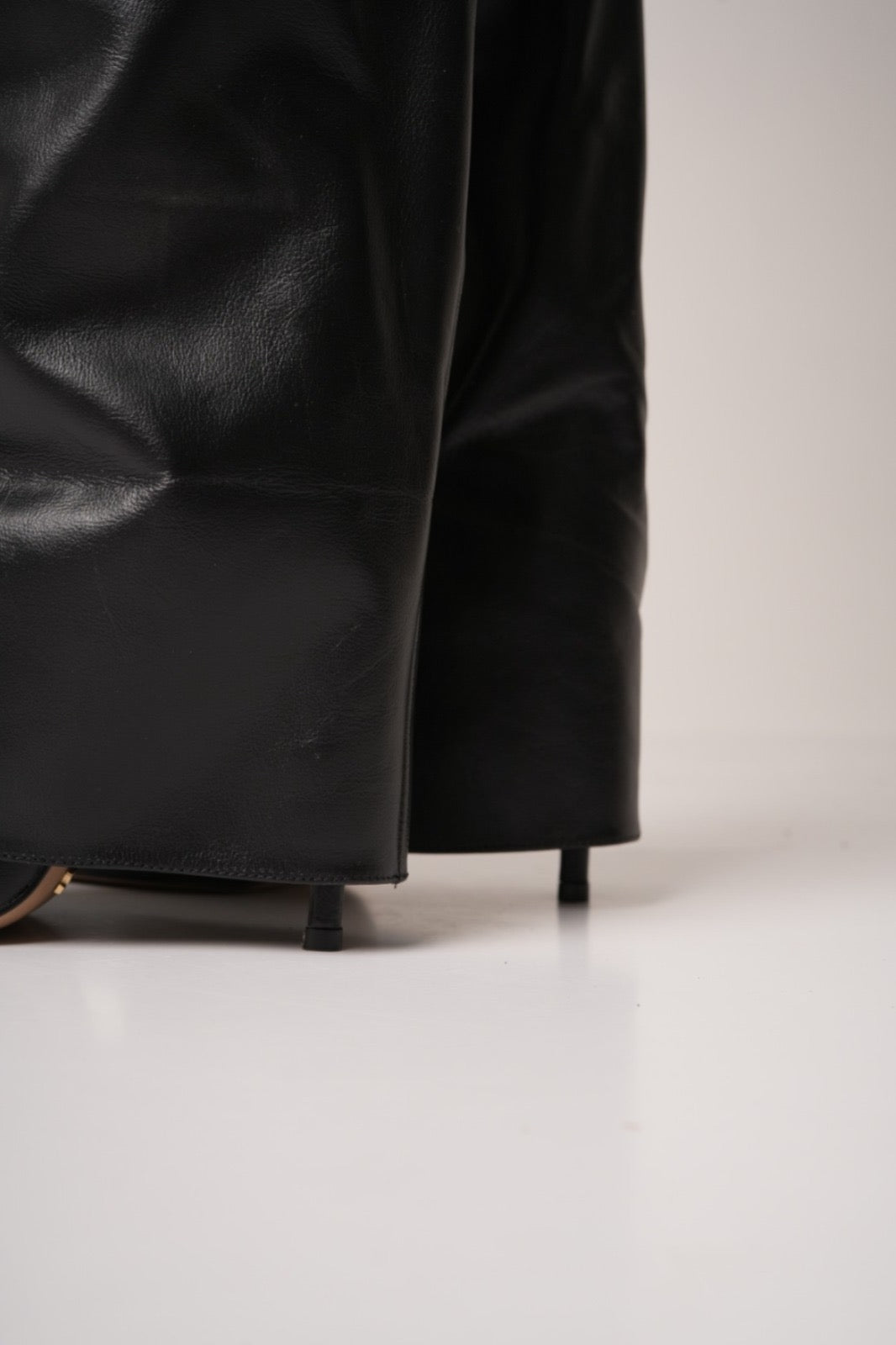 Elegant black knee-high stiletto boots with pointed toes, slouchy leather texture, and a gold padlock detail at the ankle. These statement boots blend luxury and edge—perfect for high-fashion looks or a bold night out.