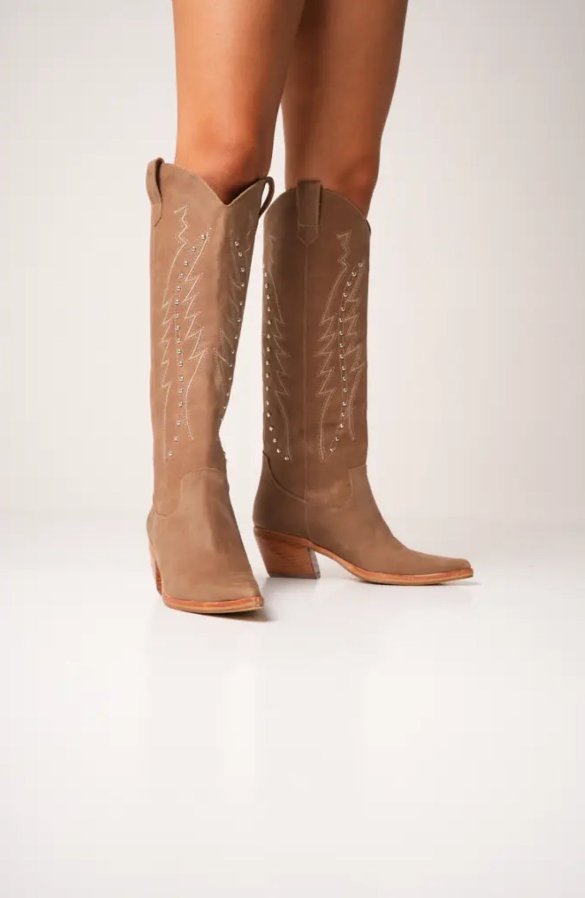 Classic tall tan cowboy boots with pointed toes, angled block heels, and intricate tonal embroidery on the shaft. A timeless Western silhouette with a sleek, all-black finish for versatile, edgy styling.