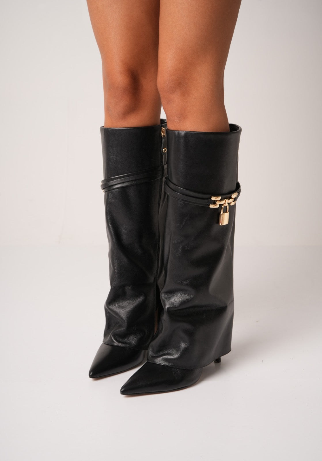 Elegant black knee-high stiletto boots with pointed toes, slouchy leather texture, and a gold padlock detail at the ankle. These statement boots blend luxury and edge—perfect for high-fashion looks or a bold night out.