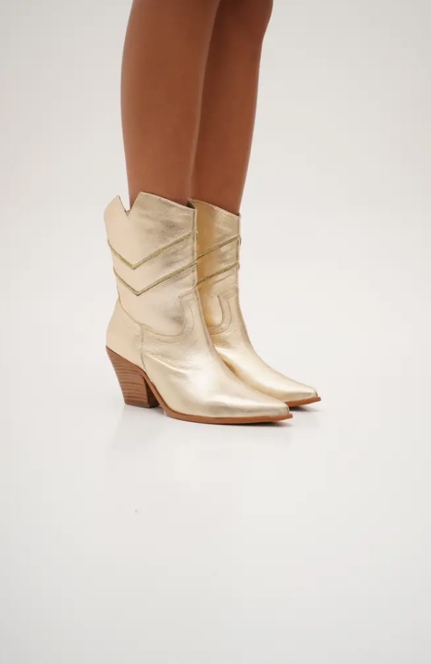 Sleek gold mid-calf cowboy boots with pointed toes, angled block heels, and silver embroidered chevron stitching. These modern western boots blend classic style with a chic, minimalist edge.