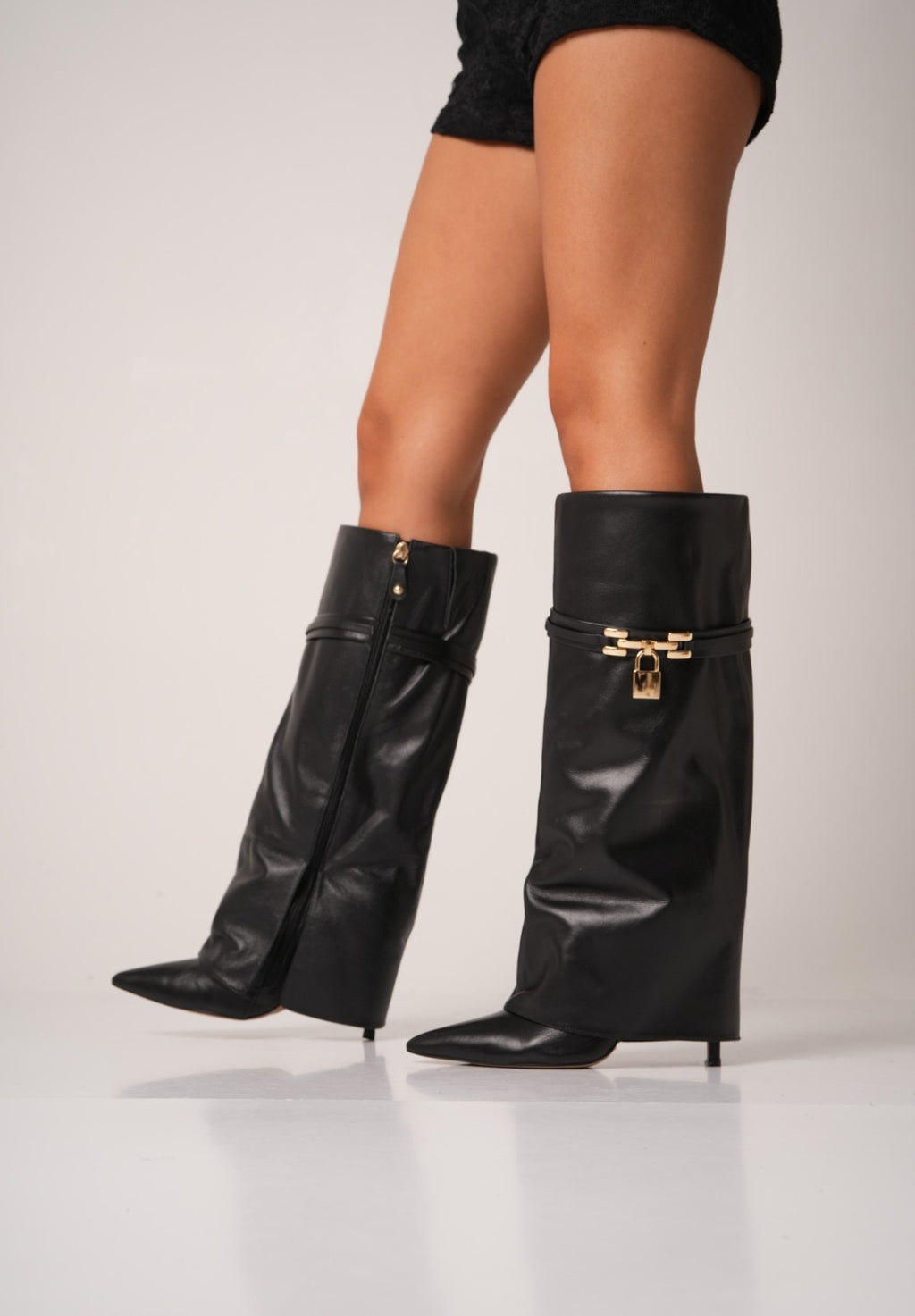 Elegant black knee-high stiletto boots with pointed toes, slouchy leather texture, and a gold padlock detail at the ankle. These statement boots blend luxury and edge—perfect for high-fashion looks or a bold night out.
