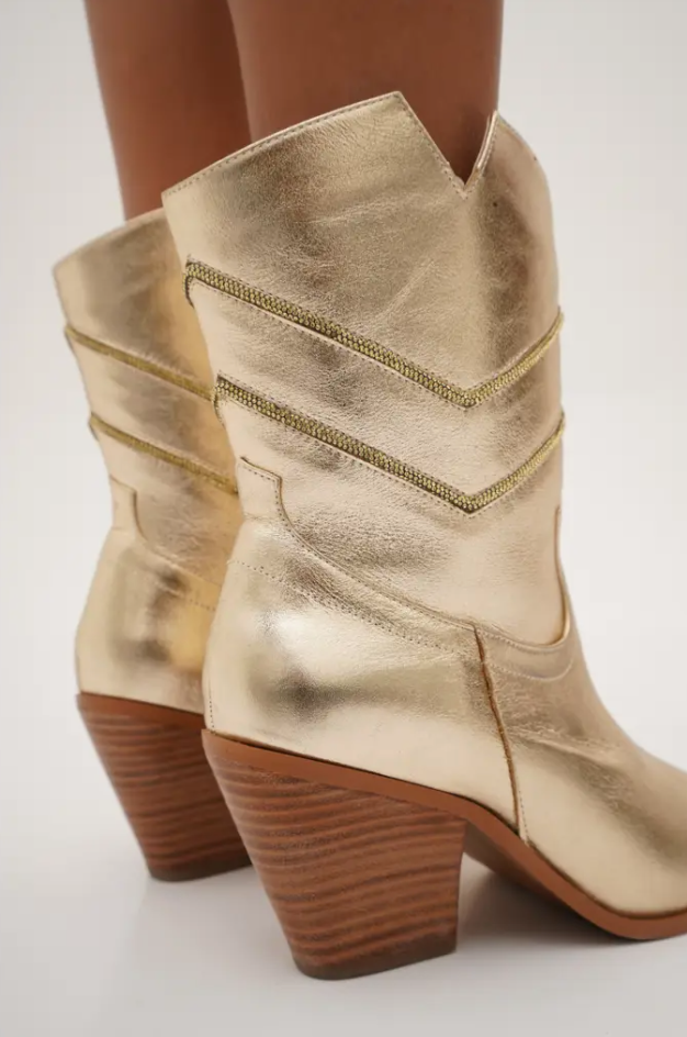 Sleek gold mid-calf cowboy boots with pointed toes, angled block heels, and silver embroidered chevron stitching. These modern western boots blend classic style with a chic, minimalist edge.
