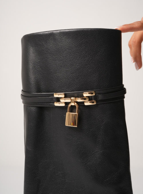 Elegant black knee-high stiletto boots with pointed toes, slouchy leather texture, and a gold padlock detail at the ankle. These statement boots blend luxury and edge—perfect for high-fashion looks or a bold night out.