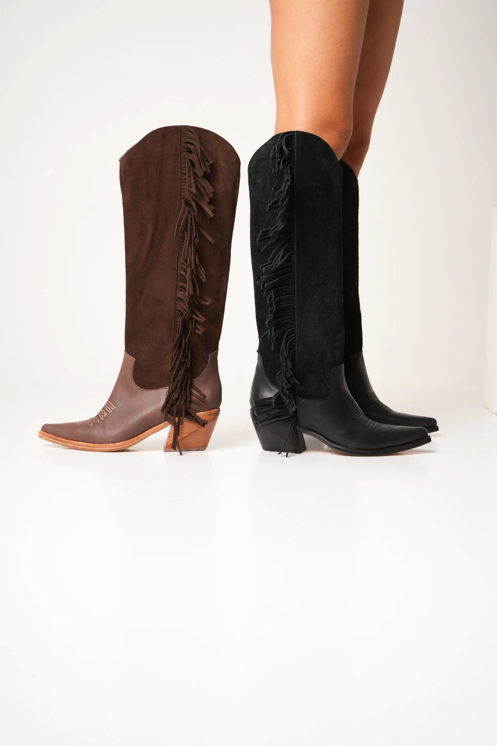 Women's tall black and brown chocolate western boots with fringe details, pointed toe, and mid heel, styled for a bold cowgirl fashion look